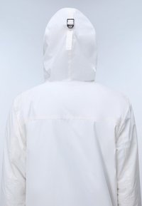 Rückansicht einer Person, die eine weiße Kapuzenjacke mit einem Riemen und einer Metallschnalle auf der Rückseite der Kapuze trägt.