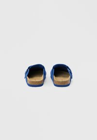 Μπλε σανδάλια χωρίς δέσιμο με πάτους από φελλό και ρυθμιζόμενα λουράκια, απεικονιζόμενα από πίσω σε απλό ανοιχτό γκρι φόντο.