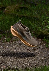 Brown athletic shoe with a mesh upper, sleek design, rubber outsole, and light beige accents; features a logo and subtle blue detailing.