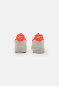Las deportivas Nike Air cuentan con una parte superior de cuero gris claro, una lengüeta trasera de color naranja brillante, forma redondeada y suela de goma texturizada.