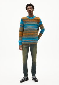 Strickpullover mit blauen, orangen und braunen horizontalen Streifen; runder Ausschnitt; kombiniert mit ausgebleichten grünen Jeans und schwarzen Schuhen.