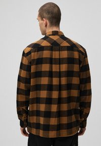 Koszula flanelowa w kratę w odcieniach brązu i czerni, z zapięciem na guziki, długimi rękawami i kształtującym tyłem. Teksturowany materiał.