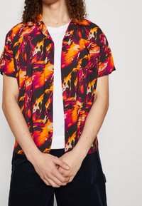 Lyhythihainen paita mustalla pohjalla, jossa on eloisat oranssi-, pinkki- ja punaisena abstraktit kuviot, napitettava malli ja rento istuvuus.