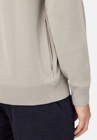 Jasnoszary sweter z teksturowanym splotem, prążkowanymi ściągaczami i bocznymi kieszeniami na zamek dla zwiększenia funkcjonalności.