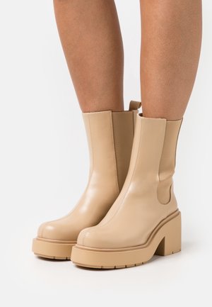 Bottes de cheville à plateforme beige avec une finition en cuir lisse et des panneaux latéraux élastiques. Talon épais avec une semelle texturée pour l'adhérence.