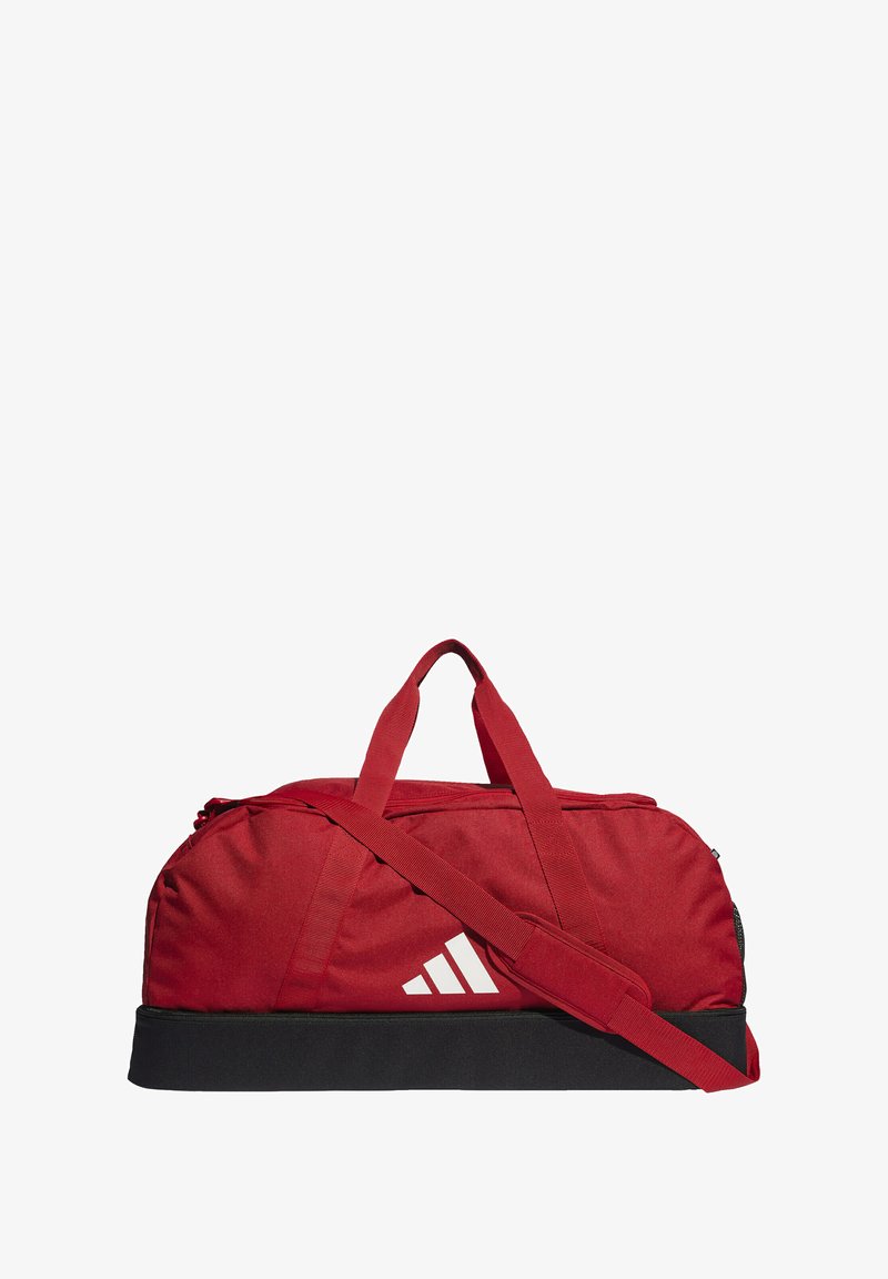 Bolsa de deporte roja con cierre de cremallera, correa de hombro ajustable, asas de tela y un fondo negro. Presenta un logo blanco en el lateral.