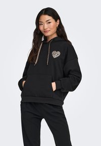 Sudadera con capucha negra con un corazón con patrón de cebra en el pecho, capucha con cordones y bolsillo delantero. Material suave, ajuste holgado.