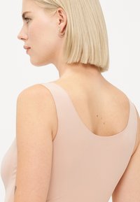 Lichtroze mouwloos bodysuit met een zachte textuur en een ronde halslijn, die de silhouet van de rug en de schoudervorm accentueert.