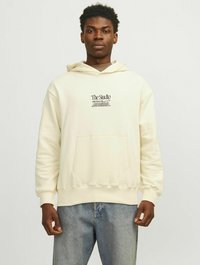 Cremefarvet hoodie lavet af blødt stof, med en lomme foran og et grafisk print på brystet. Sammen med lyseblå jeans.