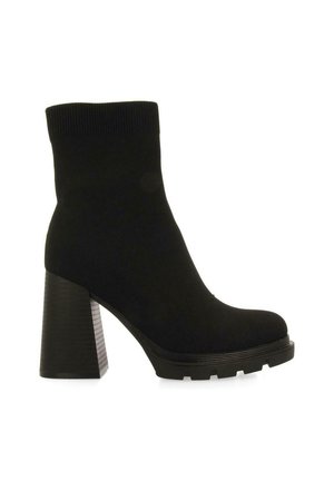 Bota de tobillo estilo calcetín negra con un grueso tacón de bloque y suela texturizada. Fabricada con un tejido suave, presenta una silueta elegante y punta redondeada.