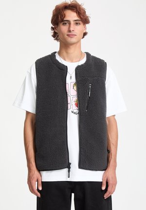 Grau gefütterte Weste mit einer Reißverschlusstasche auf der Brust, rundem Ausschnitt und einem weichen, strukturierten Finish, kombiniert mit einem weißen Grafik-T-Shirt.
