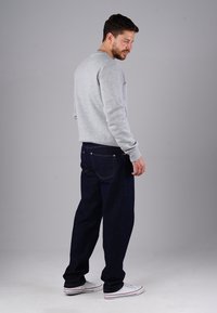 Grauer Pullover, dunkelblaue Jeans und weiße Sneakers. Der Pullover hat einen Rundhalsausschnitt und gerippte Bündchen. Die Jeans verfügen über Gesäßtaschen und sichtbare Nähte.