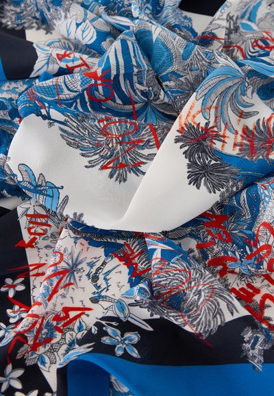 Ύφασμα με μπλε και μαύρα λουλουδένια σχέδια και κόκκινες αφηρημένες γραμμές σε λευκό φόντο, εμφανιζόμενο σε μαλακές πτυχώσεις.