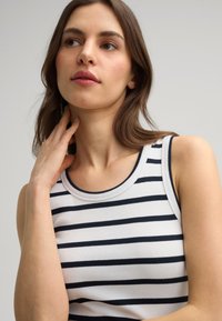 Witte tanktop met marineblauwe horizontale strepen, geribbelde textuur en een ronde halslijn. Het kledingstuk heeft brede schouderbanden.