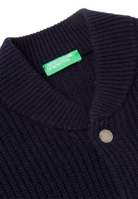Námořnický pletený svetr s ribovanou texturou, který má zelený štítek s nápisem „UNITED COLORS OF BENETTON“ a stříbrný detail knoflíku.