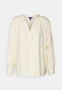 Blusa de manga longa amarela clara com uma abertura, frente abotoada e detalhes franzidos nos ombros. Confeccionada em tecido texturizado.