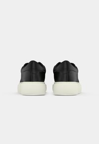 Black sneakers with a smooth finish, featuring a rounded toe, contrasting white rubber sole, and padded collar for comfort.