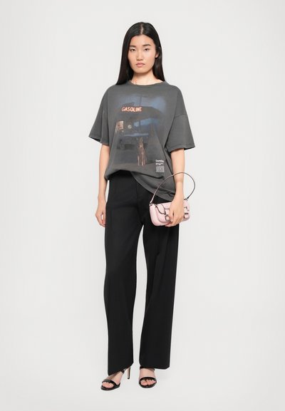 Tricou oversized gri cu un print grafic pe care scrie "GASOLINE," asortat cu pantalonii negri evazați și o geantă mică roz. Sandale cu toc negre.