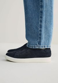 Zapatillas de ante azul marino llevadas con jeans azules, mostrando el diseño y el ajuste del zapato desde una perspectiva a nivel del tobillo.