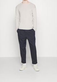Ljusbeige långärmad skjorta i kombination med mörk marinblå veckade byxor och ljusa sneakers. Outfitten har en avslappnad passform och minimal design.