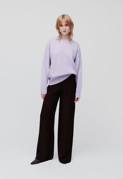 Lichtpaarse oversized trui met ribbelmanchetten, gecombineerd met zwarte wijde pantalon. Gladde textuur, minimalistisch ontwerp, geen patronen.