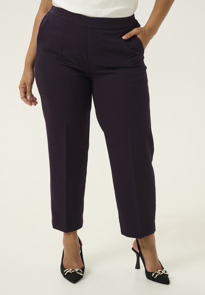 Pantaloni su misura viola con una texture liscia e una vestibilità dritta, dotati di tasche laterali. Indossati con tacchi neri a punta con accenti dorati.