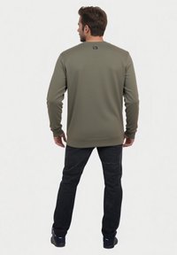 Sudadera verde oliva con tejido texturizado, cuello redondo y puños acanalados. Combinada con pantalones negros y calzado negro.