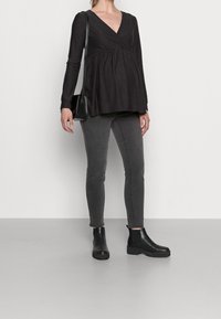 Černý dlouhý rukáv s výstřihem do V a texturovaným puntíkatým vzorem, zkombinovaný s tmavě šedými skinny džíny a černými kotníkovými botami.