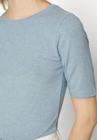 Ljusblå kortärmad T-shirt gjord av mjukt, texturerat tyg med rund halsringning och en figursydd silhuett. Inga synliga mönster eller detaljer.