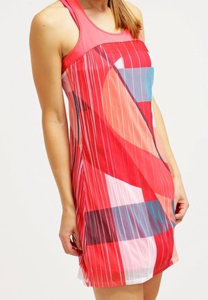 Woman wearing a sleeveless red dress with layered geometric patterns in shades of red, blue, pink, and white.
