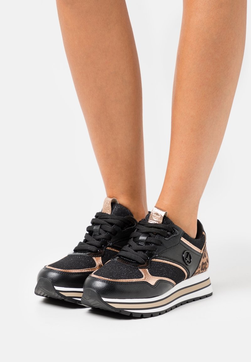 Baskets noires avec accents en or rose, tissu texturé, semelle épaisse blanche et noire, et lacets noirs. Détail imprimé léopard sur le côté.