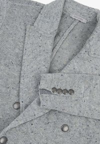 Grå spräcklig cardigan i stickat tyg, med en krage med snibb och metallknappar på ärmsluten och framknäppningen.