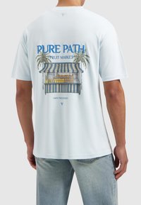 Lichtblauwe T-shirt gemaakt van zacht materiaal met een grafische print van een fruitemarkt met palmbomen en een gestreepte luifel op de achterkant.