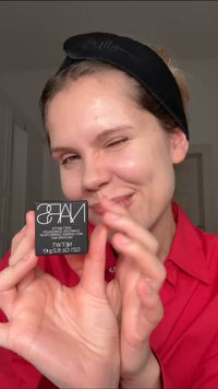 NARS Soft Matte Concealer in een zwart vierkant compact, met witte tekst, vastgehouden door een persoon in een rood shirt met een gladde, lichte huid.