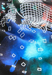 Schwarzer Stoff mit abstrakten blauen und grünen Mustern, der weiße Raster- und rechteckige Designs aufweist. Die Textur wirkt weich und glatt.