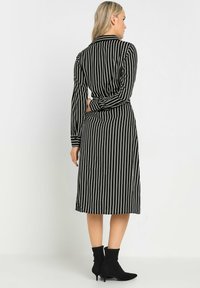 Gestreiftes schwarz-weißes Kleid mit langen Ärmeln, einem Taillengürtel und Midi-Länge, kombiniert mit schwarzen Stiefeletten. Strukturierter Stoff.