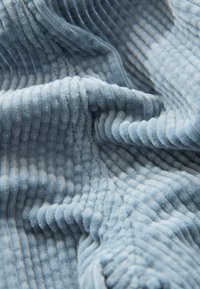 Helles blaues Cordstoff mit ausgeprägten vertikalen Rippen, weicher Textur und subtiler Glanz, in lockeren Falten angeordnet.