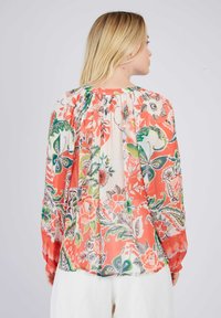 Bluse mit floralem Muster auf koralfarbenem Hintergrund, versehen mit grünen und schwarzen Mustern, langen Ärmeln und einem gerafften Ausschnitt für zusätzlichen Textur.