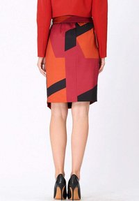 Jupe crayon à motif géométrique rouge, orange et noir, avec une fente à l'arrière, portée avec des chaussures à talons hauts noires. Texture lisse.