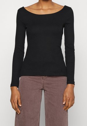 Maglietta nera a maniche lunghe con scollatura ampia, texture a coste e design aderente. Abbinata a pantaloni marroni a vita alta.
