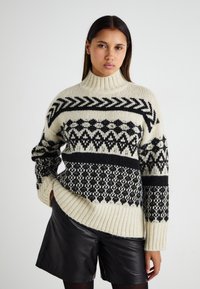 Kreemikas turtleneck'iga sviiter mustade geomeetriliste mustritega, millel on ribatud mansetid ja äär, kantud mustade nahkšortsidena.