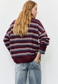 Pulover cu dungi vișinii, cu dungi albe și albastre, tiv și manșete tip rețea, asortat cu blugi din denim bleu deschis, cu croială lejeră.