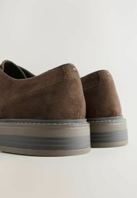Chaussures en daim marron avec une finition texturée, dotées d'une semelle grise épaisse et de surpiqûres blanches le long du bord.