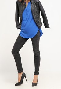 Giacca di pelle nera, blusa blu con pattina dei bottoni, jeans neri skinny e scarpe nere con tacco alto. Cuffie arrotolate sui jeans.