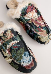 Hausschuhe mit Blumenmuster, bestehend aus einem schwarzen, gewebten Stoffboden und cremefarbenem Kunstfellbesatz, mit einem Schlupfdesign und abgerundeter Form.