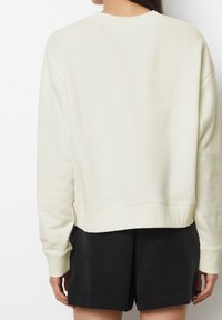 Sudadera de crema clara con corte relajado, puños acanalados y dobladillo recto, combinada con pantalones cortos negros. Textura suave y diseño minimalista.