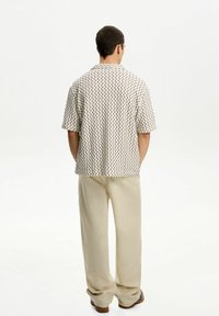 Kortärmad skjorta i krämfärg med ett svart zickzackmönster; matchad med ljusbeiga vida byxor. Slät textur, avslappnad passform.