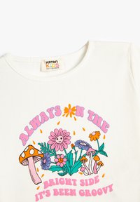 Hvid ribbet børnet-shirt med farverige blomster- og svampe grafik samt teksten "Altid på den lyse side, det har været groovy."