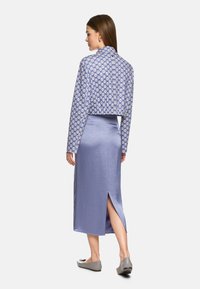 Gekürzte Jacke mit blau-weißer Blumenmuster, kombiniert mit einem lila Satinrock mit Schlitz hinten und minimalistischen grauen Flats.
