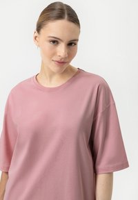 T-shirt rosa a maniche corte con scollatura rotonda, texture morbida, vestibilità rilassata e spalle senza cuciture, esposto su uno sfondo chiaro.